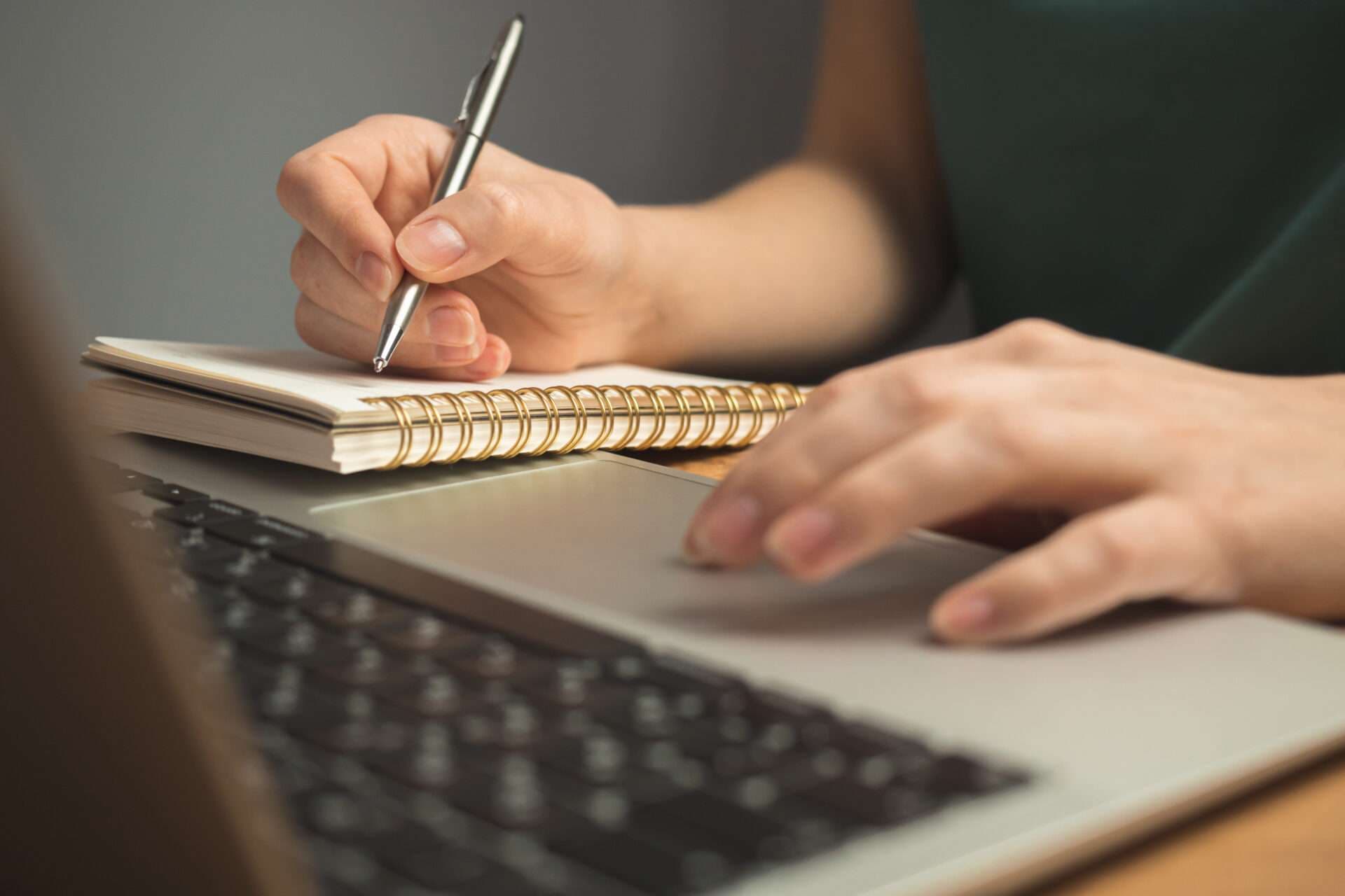 A person writing in a spiral notebook resting on a laptop keyboard.