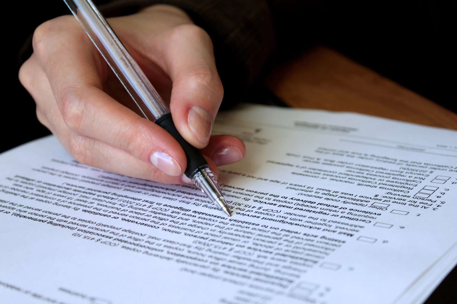 A hand filling in a printed legal form with a ballpoint pen.